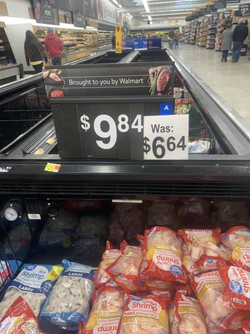 Grocery store freezer with shrimp bags and a humorous price sign.
