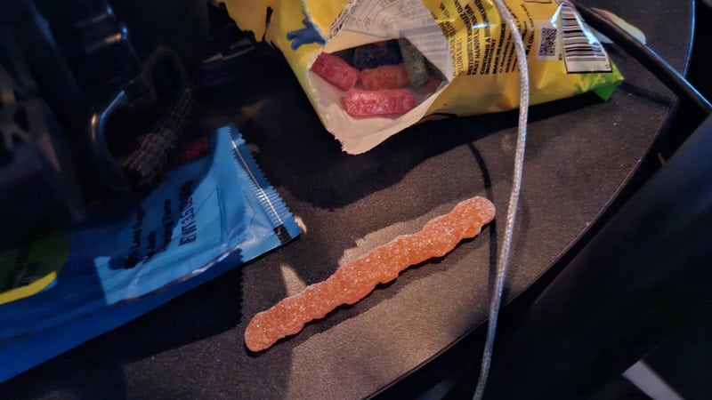 Close-up of a gummy worm candy on a dark desk surface.