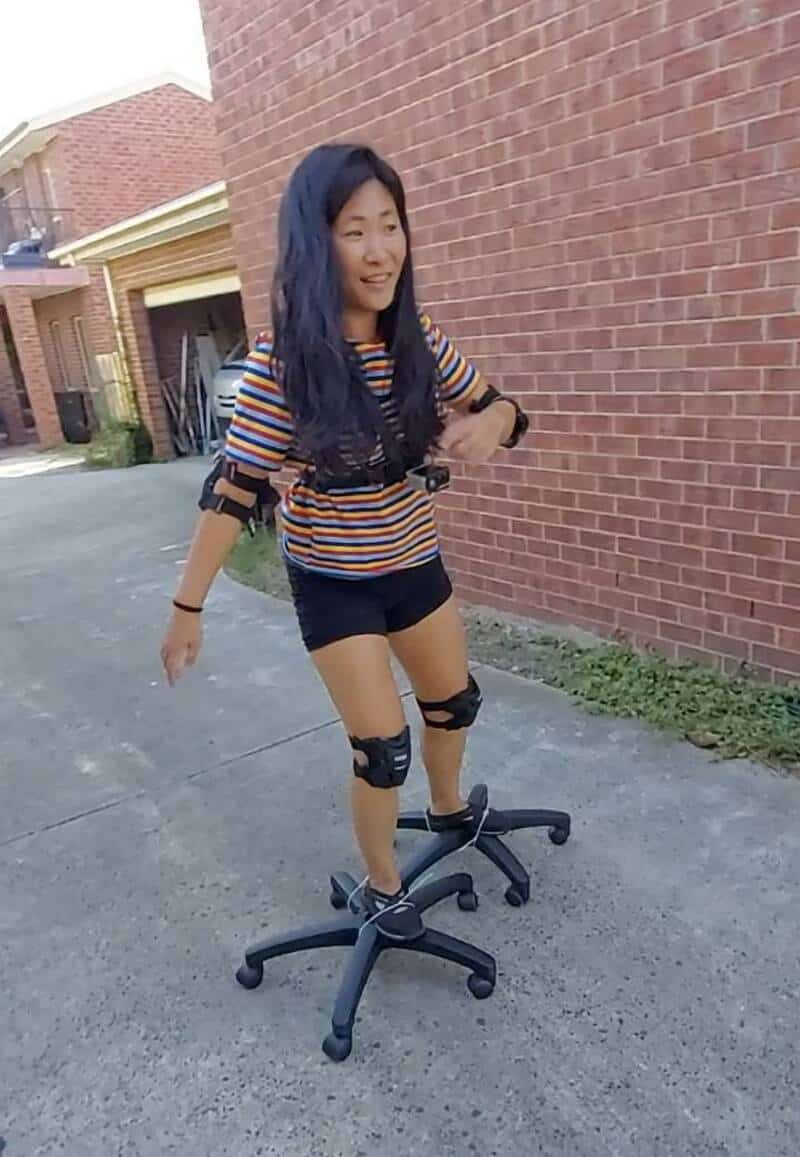 Woman with long dark hair balancing on an office chair outside, smiling.
