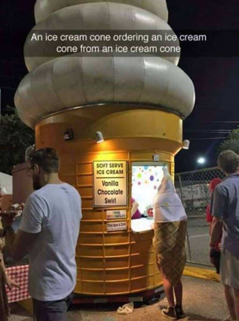 People ordering ice cream from a giant ice cream cone stand at night.