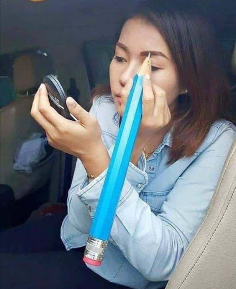 Woman using a giant pencil as a makeup brush in a car interior.