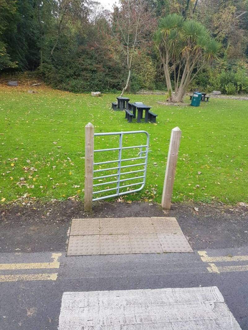 Playground gate leading to grassy park with benches and trees.