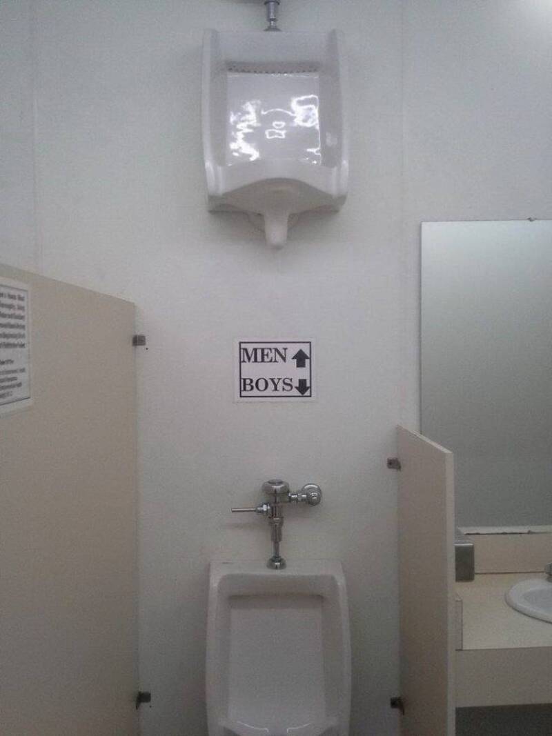 Bathroom sign with "MEN" and "BOYS" labels above a urinal.