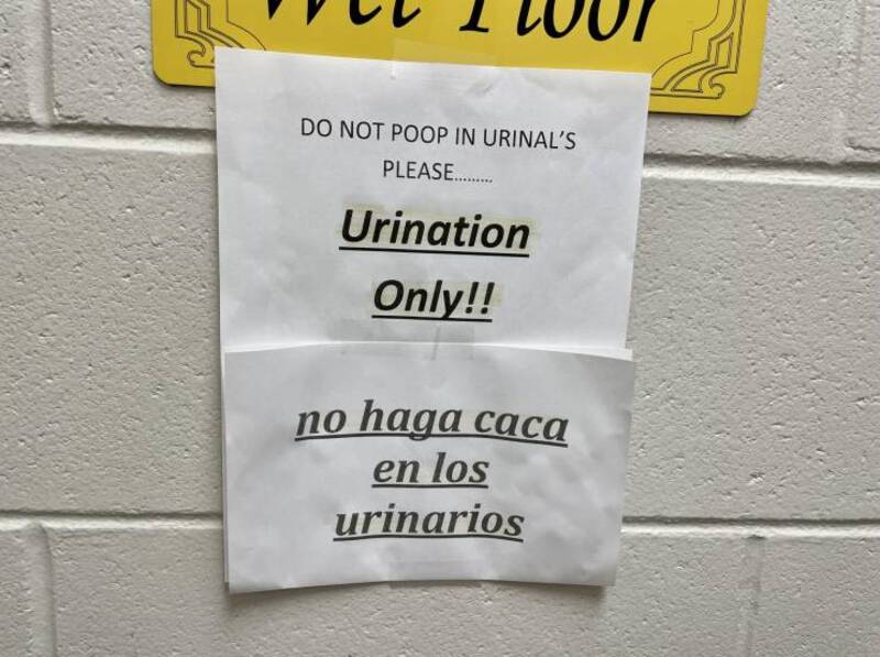 Humorous bathroom sign instructing not to poop in urinals, with bilingual message in English and Spa.