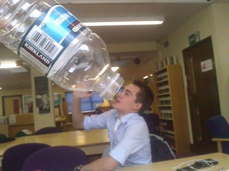 Student pretending to drink from an oversized water bottle in classroom.