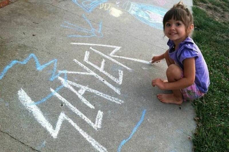 Child girl drawing with chalk on sidewalk.