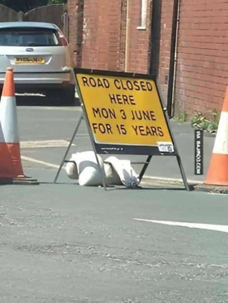Road closed sign with two swans resting at the base, blocking a street.