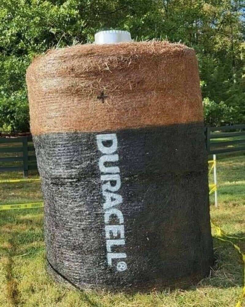 Large hay bale painted with Pleated Jeans logo in black and white outdoors.