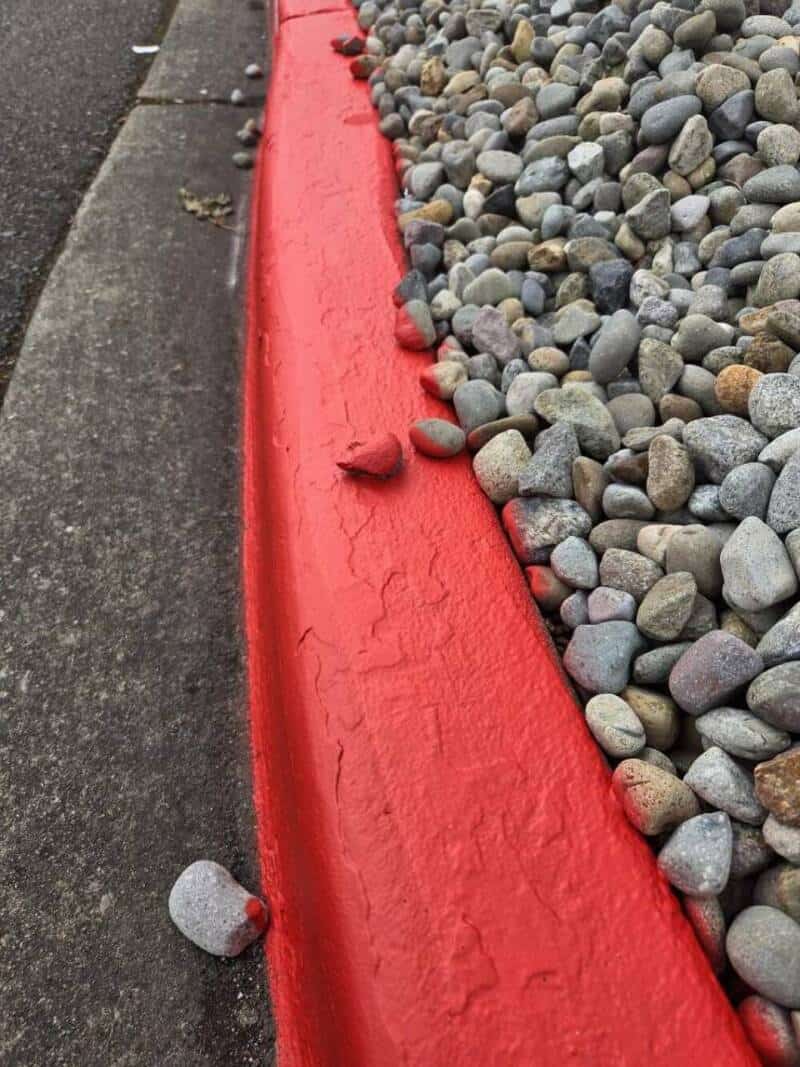 Red curb with small rocks and pebbles on the side of the sidewalk.