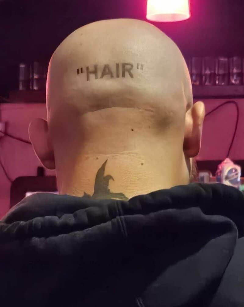 Bald man with "HAIR" tattoo on the back of his head, facing away from the camera.