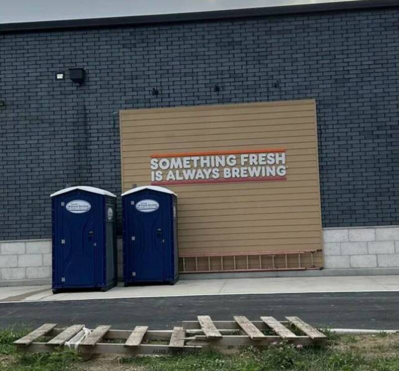 Portable toilets outside a store with a sign reading "Something fresh is always brewing".