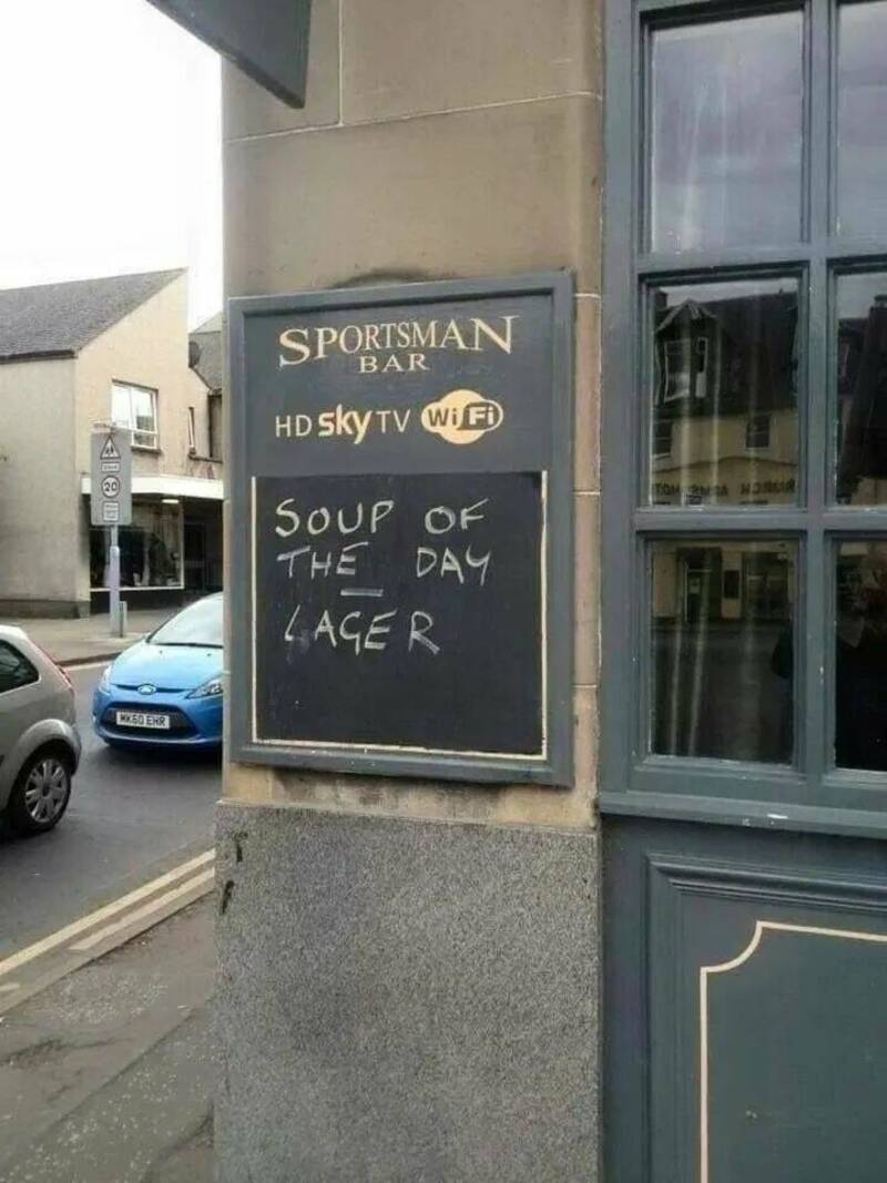 Chalkboard sign outside Sportsman Bar advertising soup of the day and lager, on a city street.