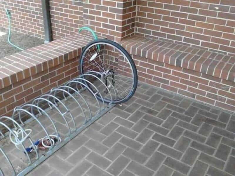 Bike rack with a bicycle wheel and brick wall background for outdoor bike storage.