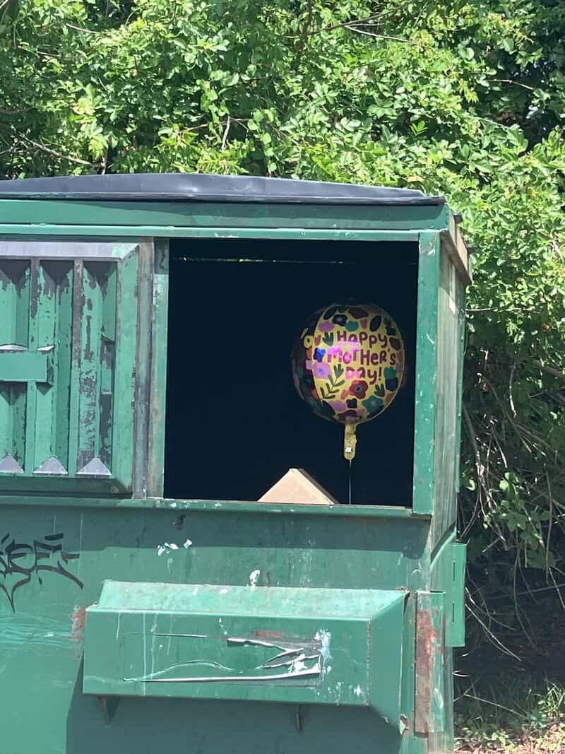 Mother's Day balloon with colorful "Happy Mother's Day" message inside a green dumpster.