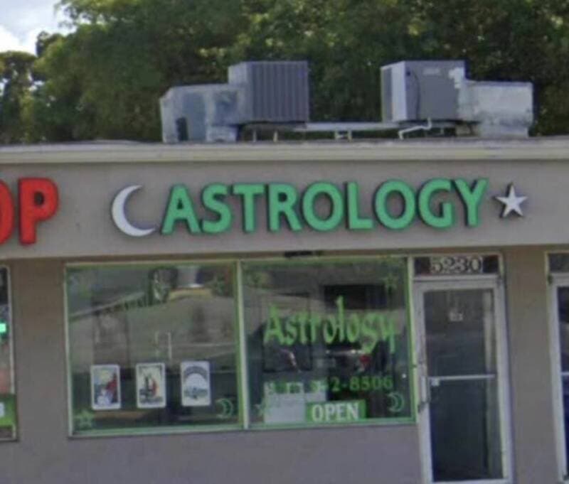 Astrology shop sign with "Astrology" in green letters and moon and star symbols, located on a storef.