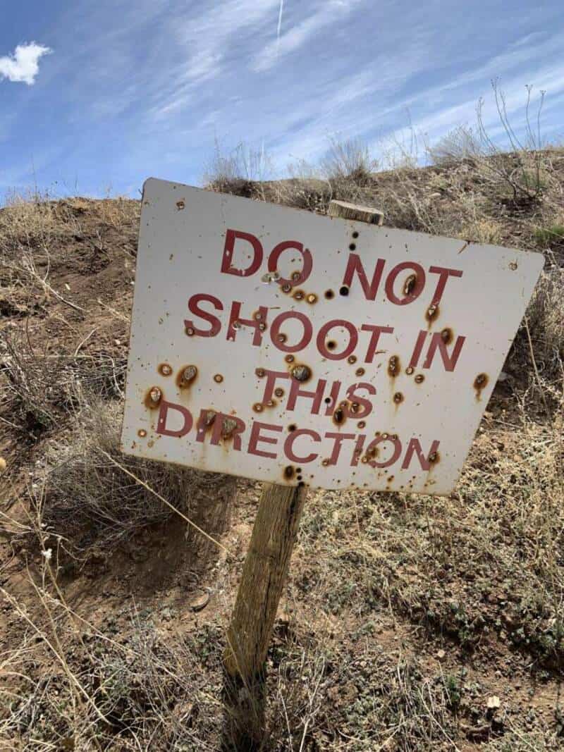 Rusty "Do Not Shoot in This Direction" sign on a dirt hill, weathered and tilted.