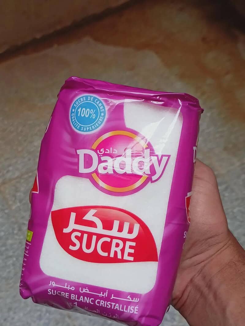 Hand holding a pink packet of "Sala Daddy" white sugar with Arabic text and branding.