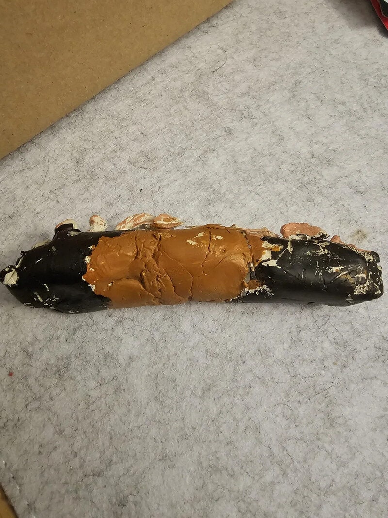 Unusual snack with chocolate coating, resembling a humorous or odd-shaped treat on a gray surface.