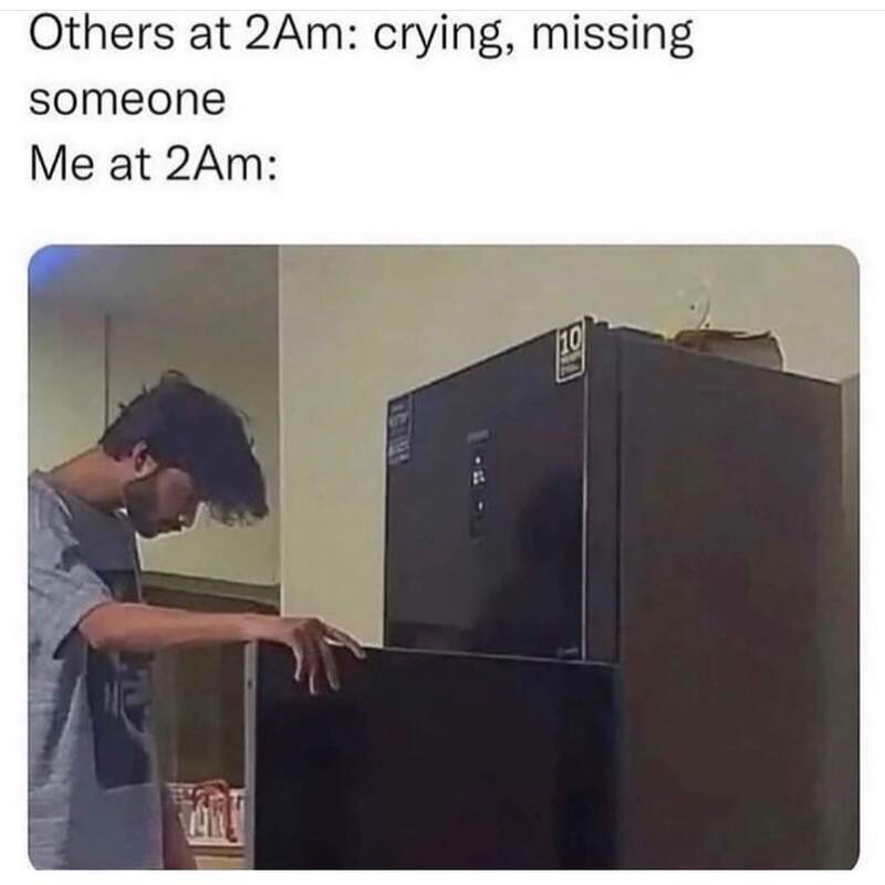 Young man looking confused at a refrigerator in a dimly lit room.