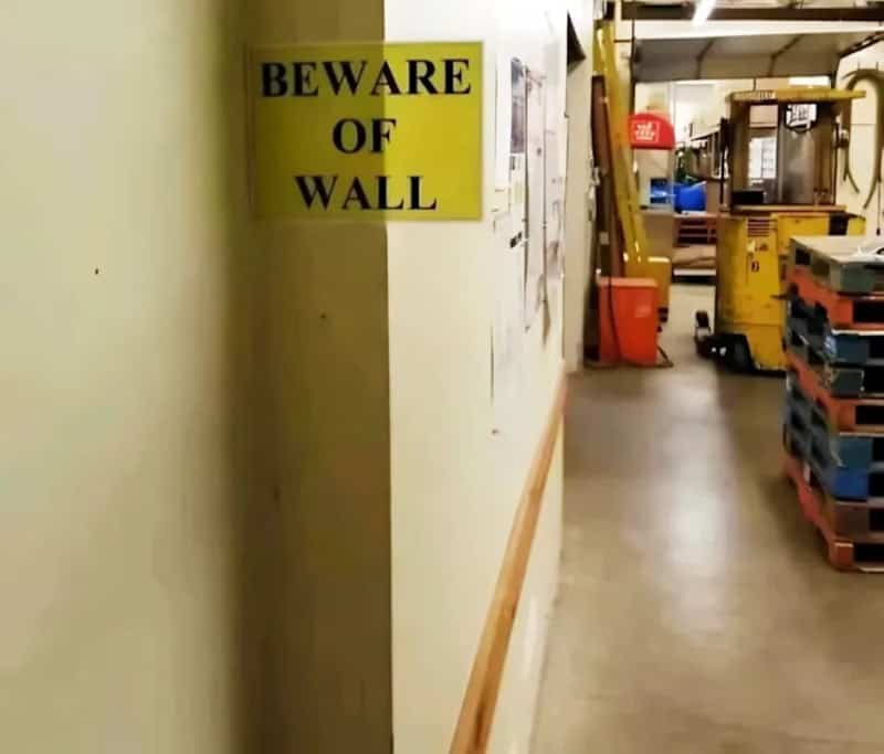Warning sign reading "BEWARE OF WALL" in bold black letters on yellow background.