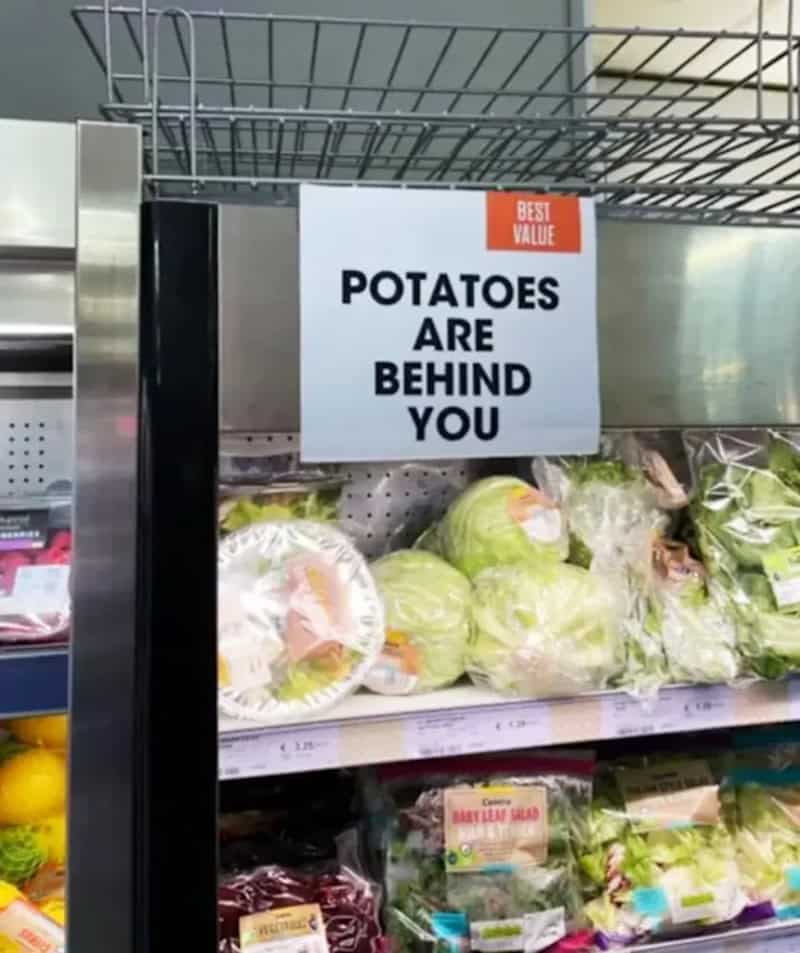 Sign in grocery store reading "Potatoes are behind you" above fresh produce.
