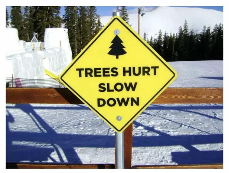 Caution sign warning about trees hurting and slowing down in a snowy outdoor setting.