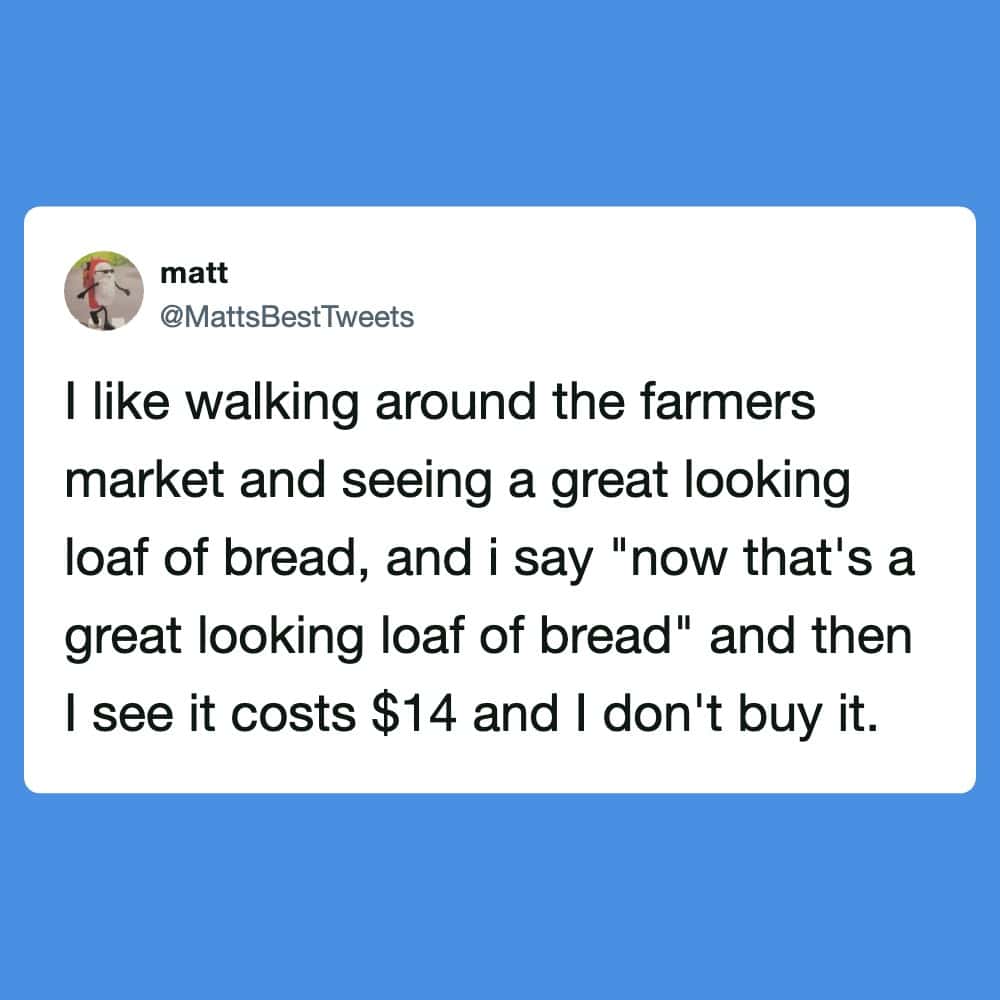 "Man walking past a farmers market stall with a loaf of bread".