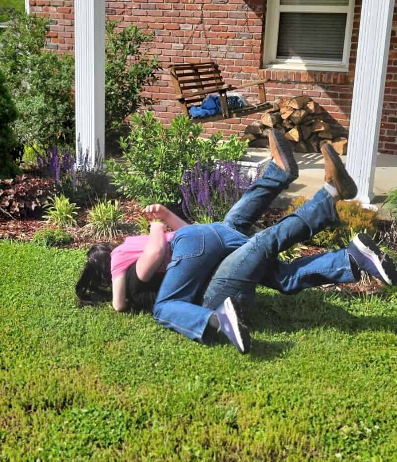 Kids wrestling and playing on green grass in backyard.