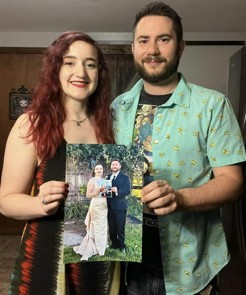 Happy couple holding a photo at a casual gathering, smiling and enjoying the moment.