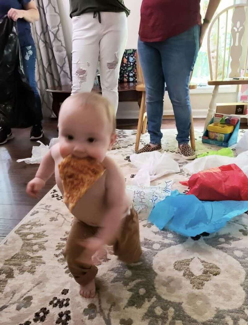 Baby with pizza slice at indoor gathering.