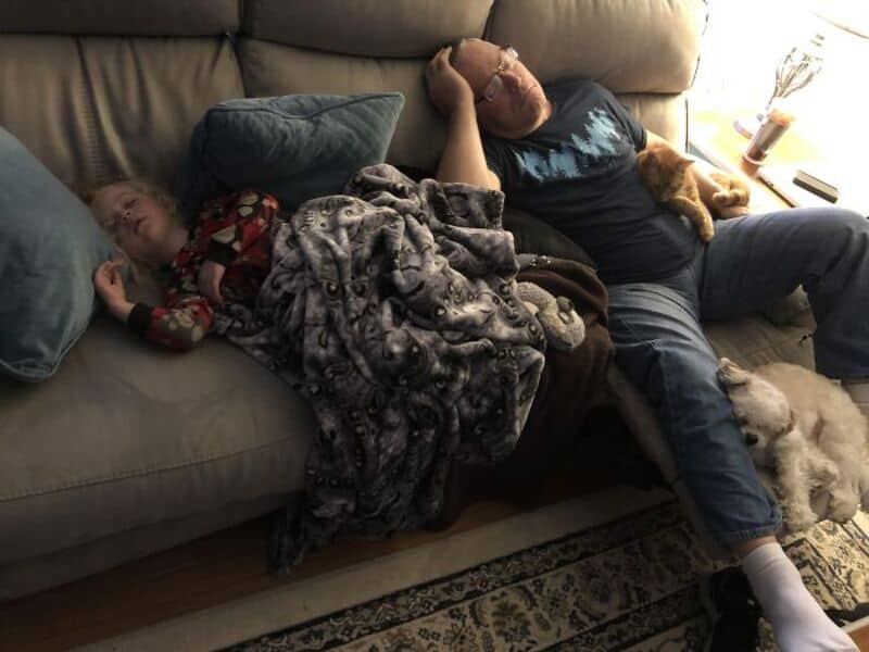 Relaxing couple napping on sofa with pets, cozy home scene.