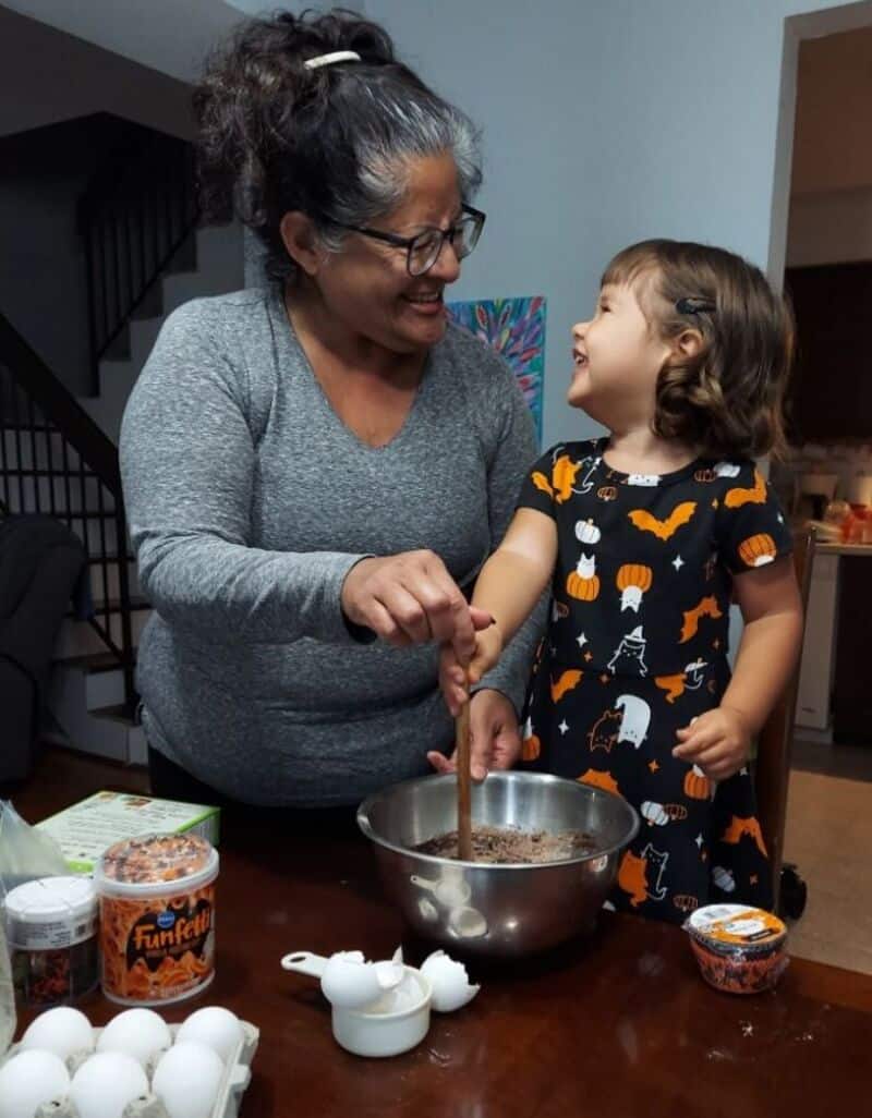 Happy woman and girl baking Halloween cookies together in kitchen.