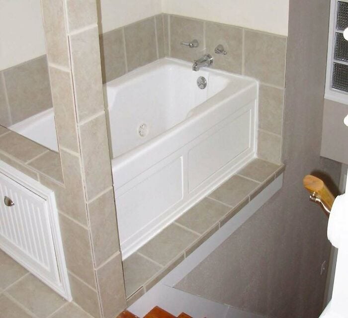 A bathtub with a tiled surround and a partial view of a bathroom.