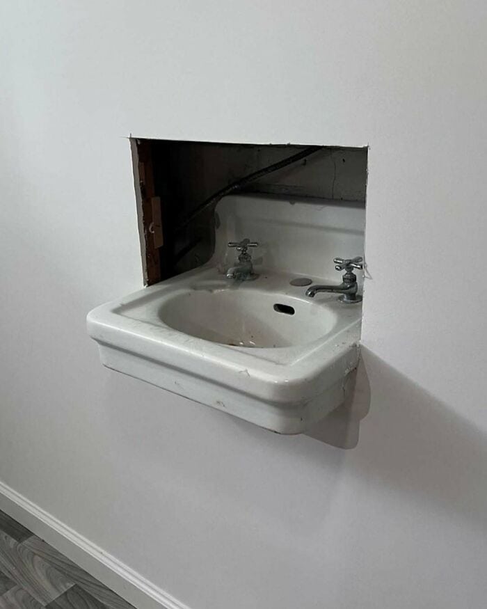 Small wall-mounted sink with two taps in a wall opening.