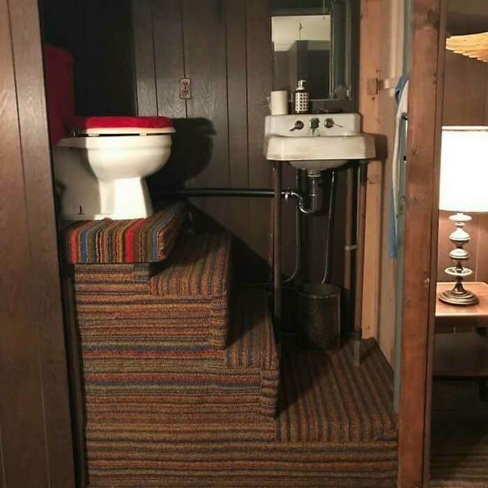 Small bathroom with toilet, sink, and striped carpeted steps.