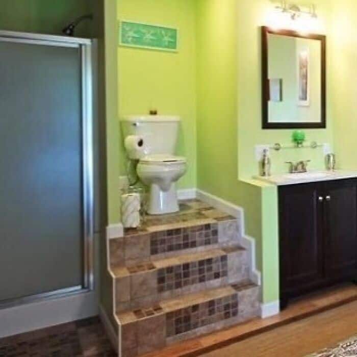 Small bathroom with green walls, toilet on raised tiled platform, and black vanity with mirror.
