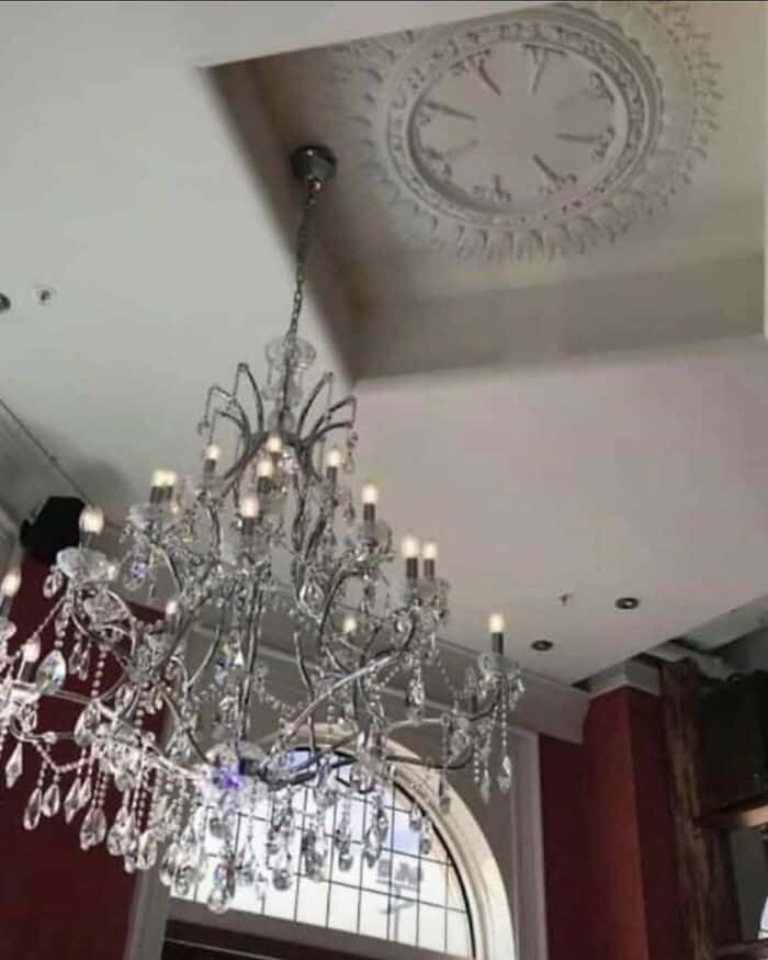 Chandelier hanging from ceiling with a clock on the ceiling in the background.