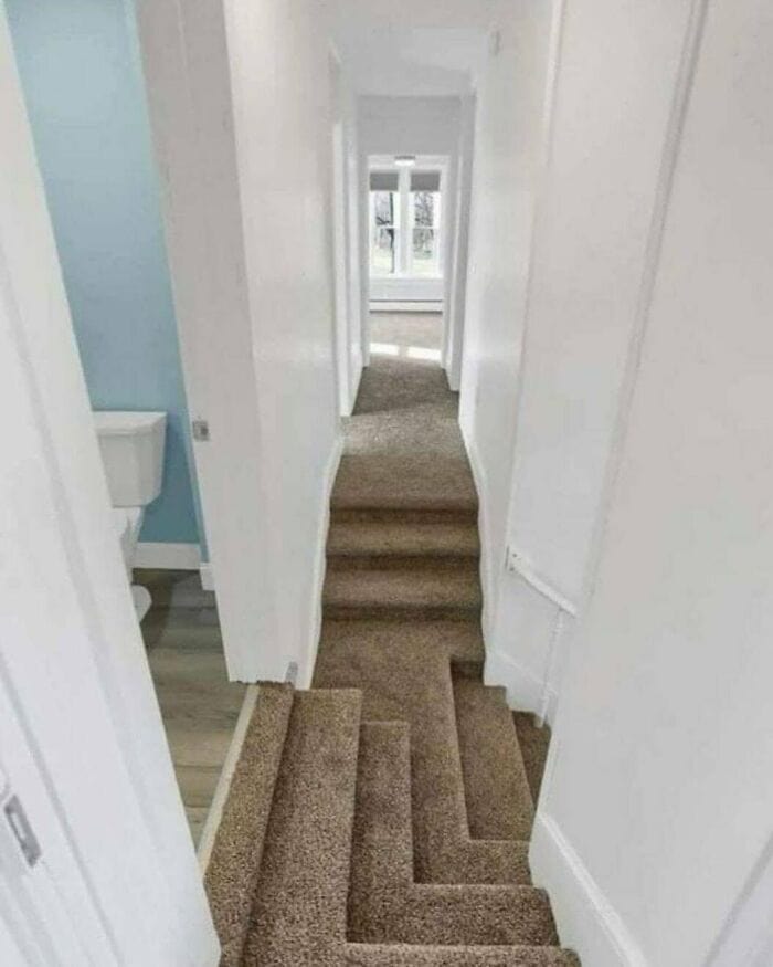 Narrow staircase with beige carpet leading to a bright room with large windows.