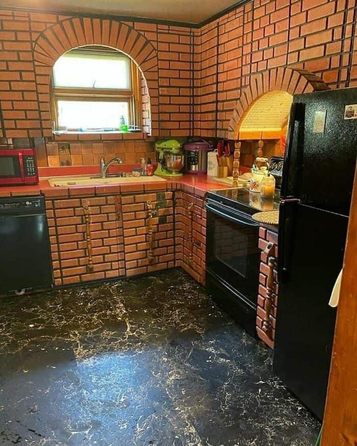 Brick kitchen with black appliances and a window above the sink.