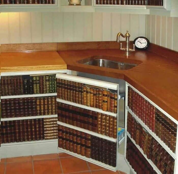 "Kitchen corner with bookshelves filled with leather-bound books, wooden countertop, sink, and clock.