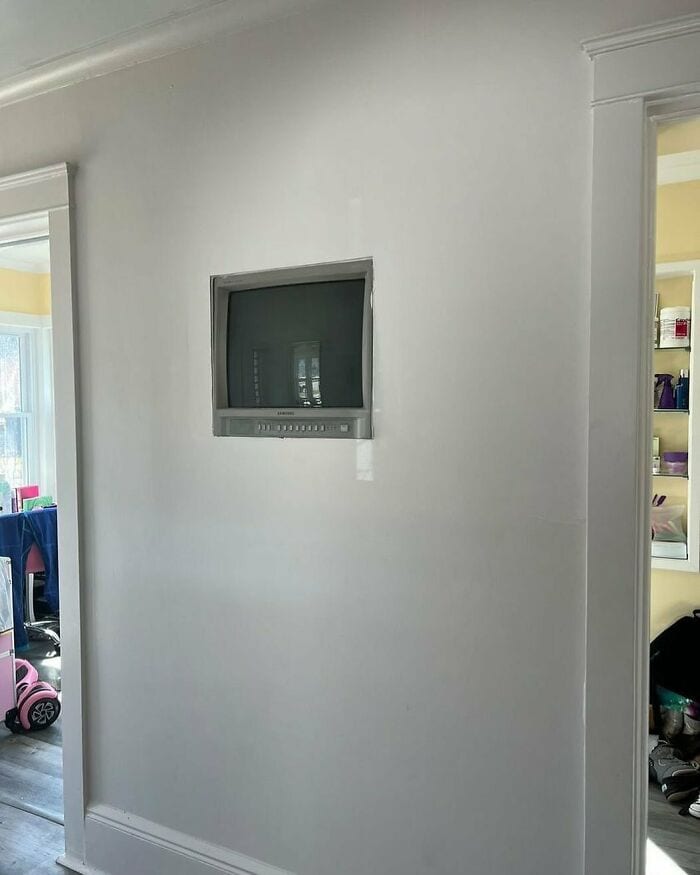 Wall-mounted TV in a bright room with a doorway to a cluttered room.