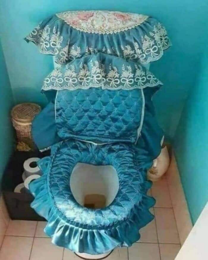 Blue decorative toilet seat cover with ruffled edges and lace details, placed on a toilet.