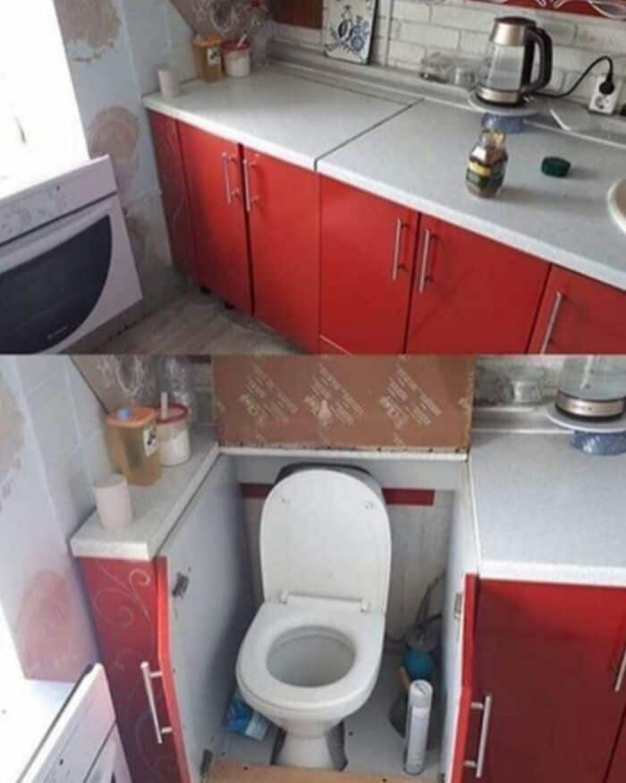 Kitchen with red cabinets and a toilet in a small space, cluttered with various items.