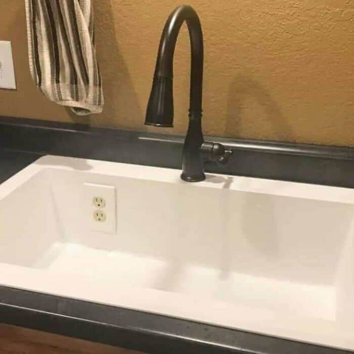 Modern kitchen sink with black faucet and striped towel hanging nearby.