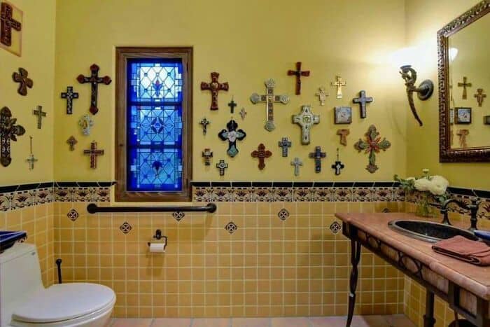Colorful wall of crosses in a bathroom with a window, sink, and mirror.