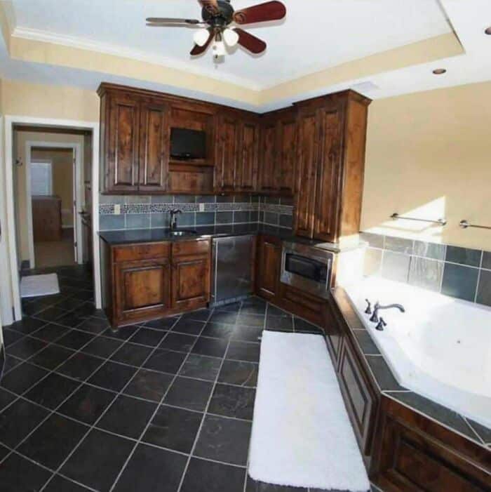 Kitchen with dark wood cabinets, black tiled floor, and a bathtub with a window.
