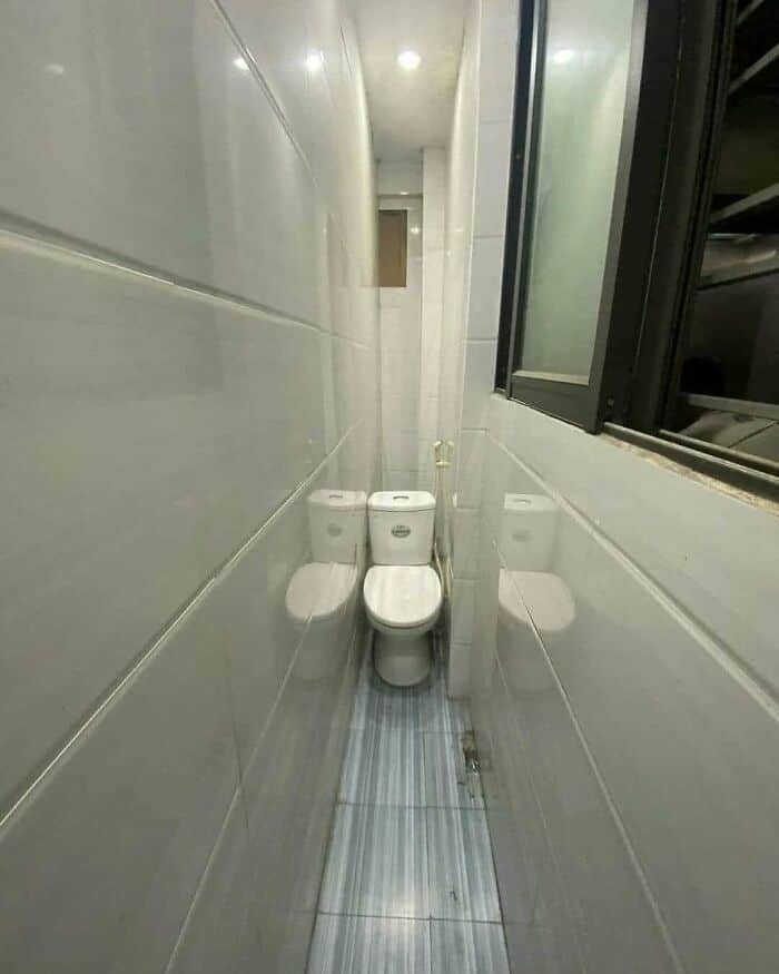 Narrow bathroom with two toilets and a window on the right side.