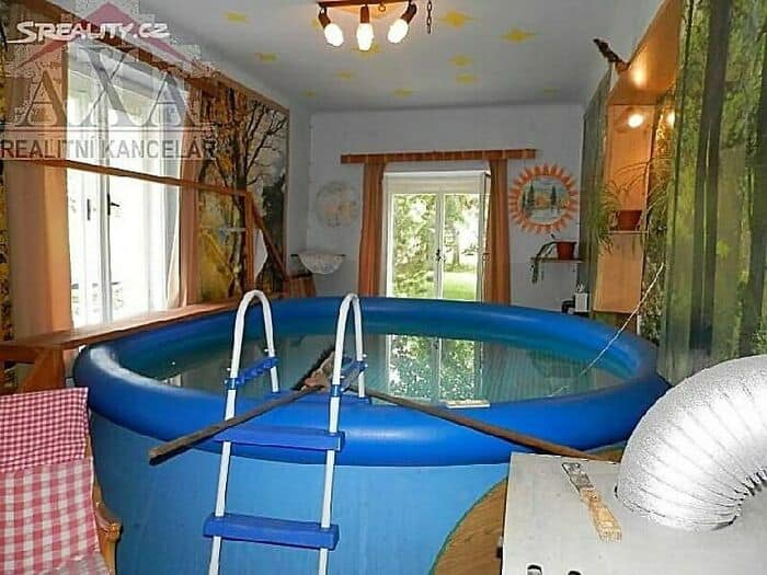 Blue inflatable pool with a ladder inside, set up indoors near windows and a door.