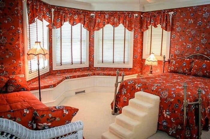 Cozy bedroom with floral red curtains, matching bedding, and a small staircase leading to the bed.