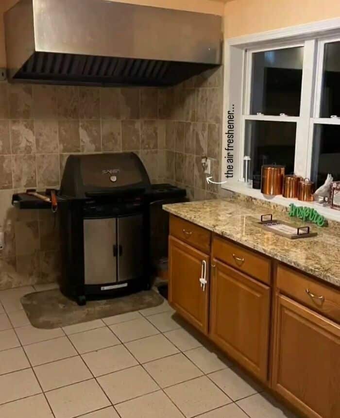 Grill in kitchen with wooden cabinets and window, "the air freshener" on the windowsill.